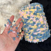 A hand holds a ball of hand-dyed variegated cotton blend yarn featuring shades of blue, yellow, and pink.