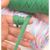 A hand is shown manipulating thick green polyester blend yarn for knitting and crochet.