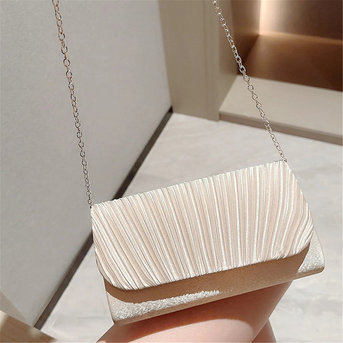 A light beige patent leather clutch bag with vertical pleats and a silver chain strap.