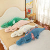 A collection of soft stuffed dragon plush pillows in green, pink, and blue resting on a bed.