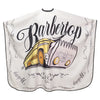 A white salon cape featuring a black script design of the word Barbertop and an illustration of a yellow and pink barber tool