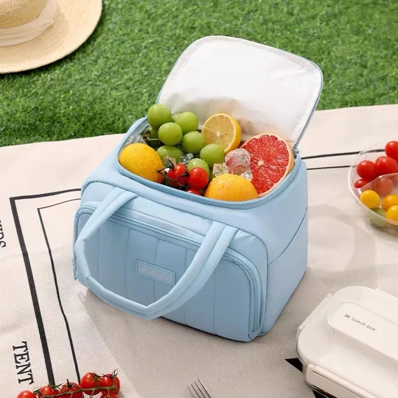 A light blue insulated quilted lunch tote bag is open, revealing fresh fruit like lemons and grapes inside.