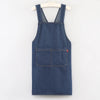 A dark indigo denim cross-back apron with a chest pocket hanging on a white hanger.