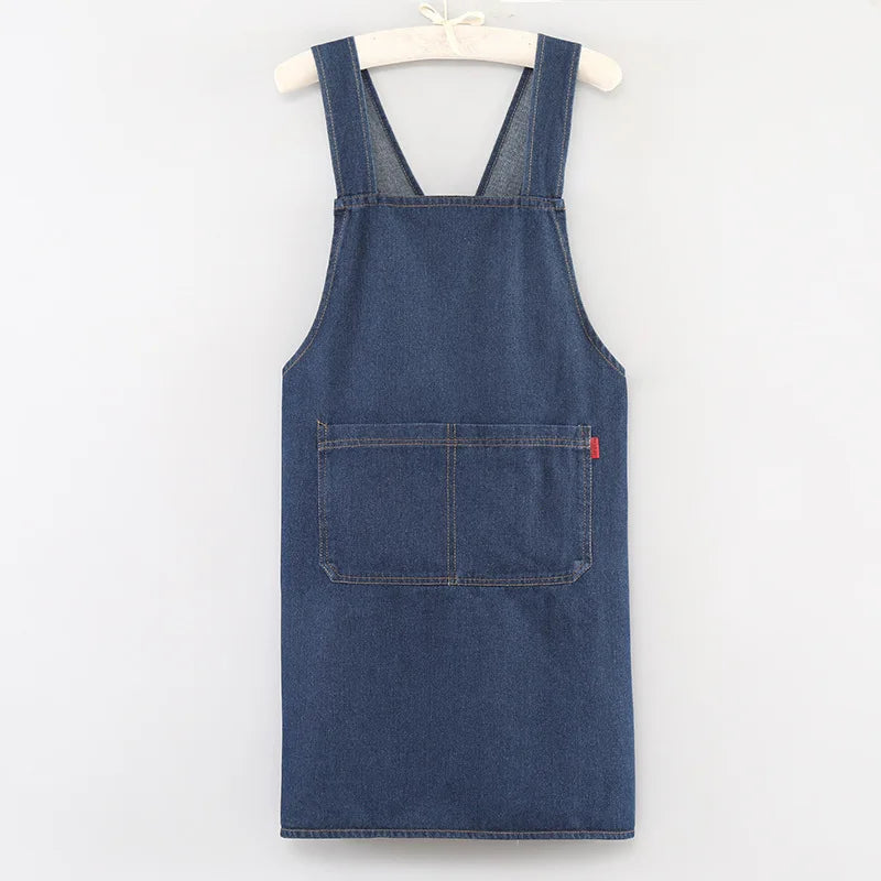 A dark indigo denim cross-back apron with a chest pocket hanging on a white hanger.