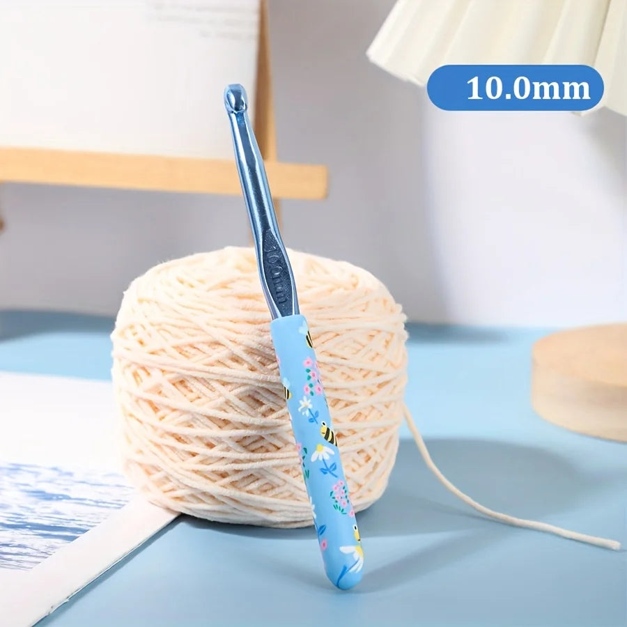 A blue ergonomic crochet hook with a bee design is shown next to a ball of light-colored yarn.