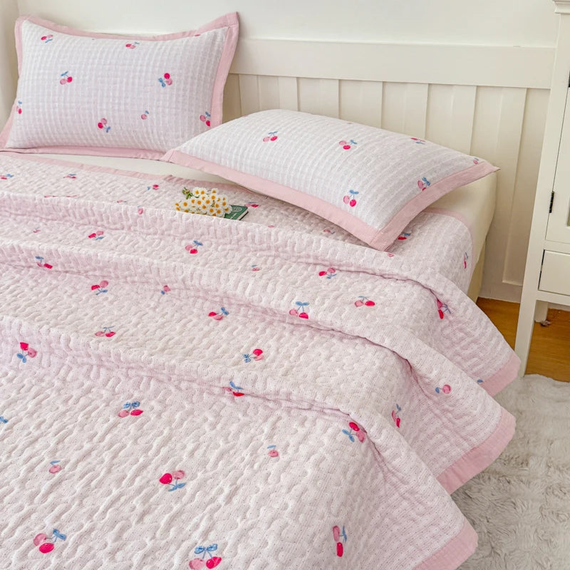 Pink quilted bedspread with floral embroidery and matching pillow on a white wooden bed frame.