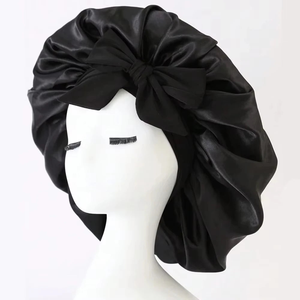 Black satin silk sleep bonnet tied in a large bow displayed on a white mannequin head.