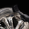 A hand using a black brush to clean dirt from a car wheel and tire.