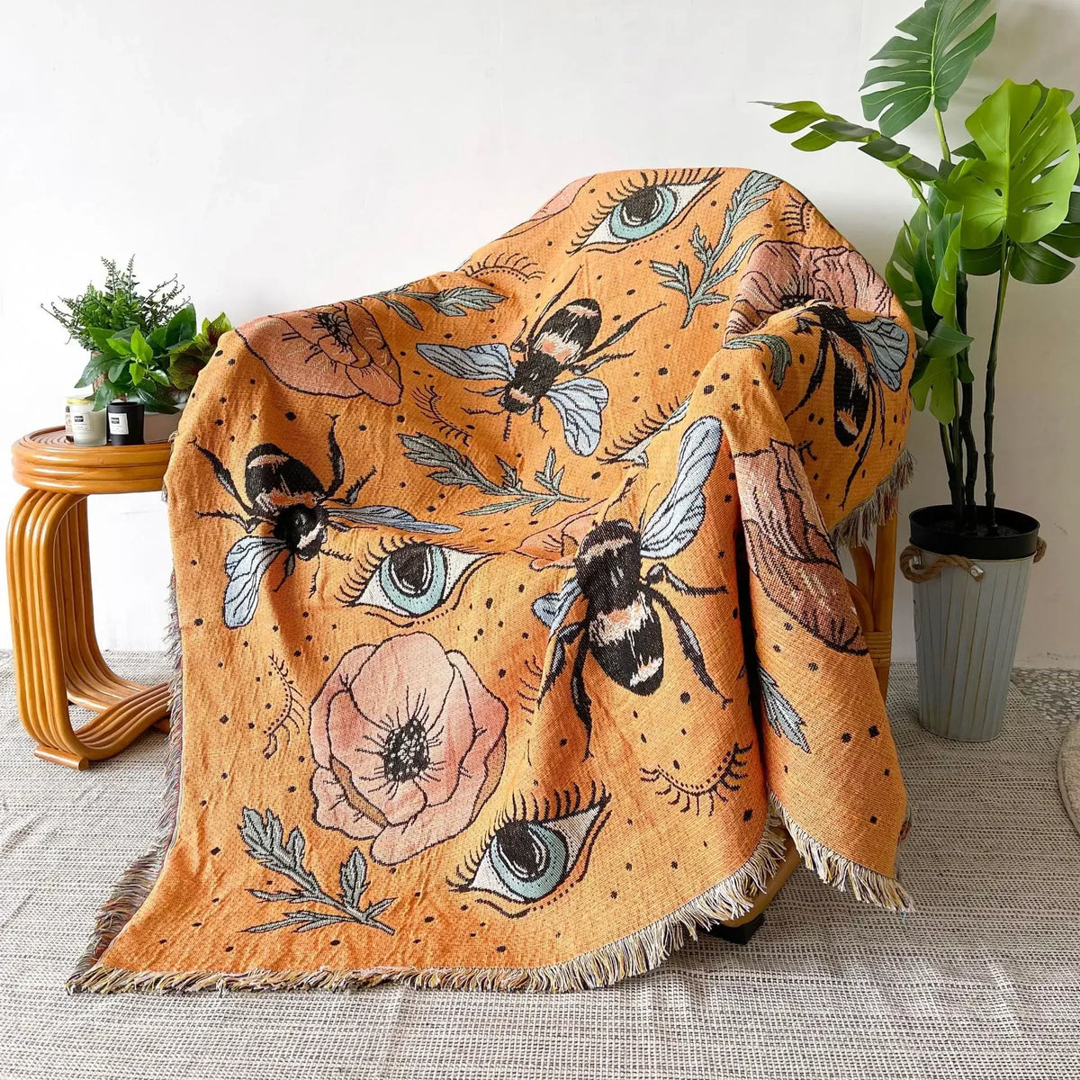 A bohemian jacquard woven throw blanket featuring an orange background with stylized bees and eyes.