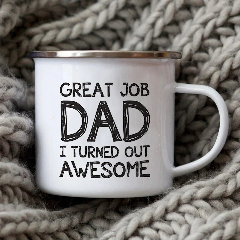 Tasse à café émaillée blanche avec bord argenté et texte noir disant « Great Job Dad I turned out Awesome », posée sur un sup