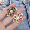 A hand holds a gold-toned adjustable flower waist clip with pearl accents against a denim background.