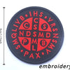 A black embroidered patch featuring the IHS monogram and the acronyms QLIVB, CNS, and others in red thread.