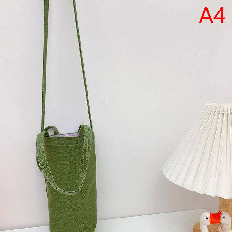 A green canvas crossbody bag hanging on a white wall.