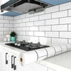 A white kitchen splashback tiled with subway tiles, featuring a stainless steel range hood above a countertop and a roll of w