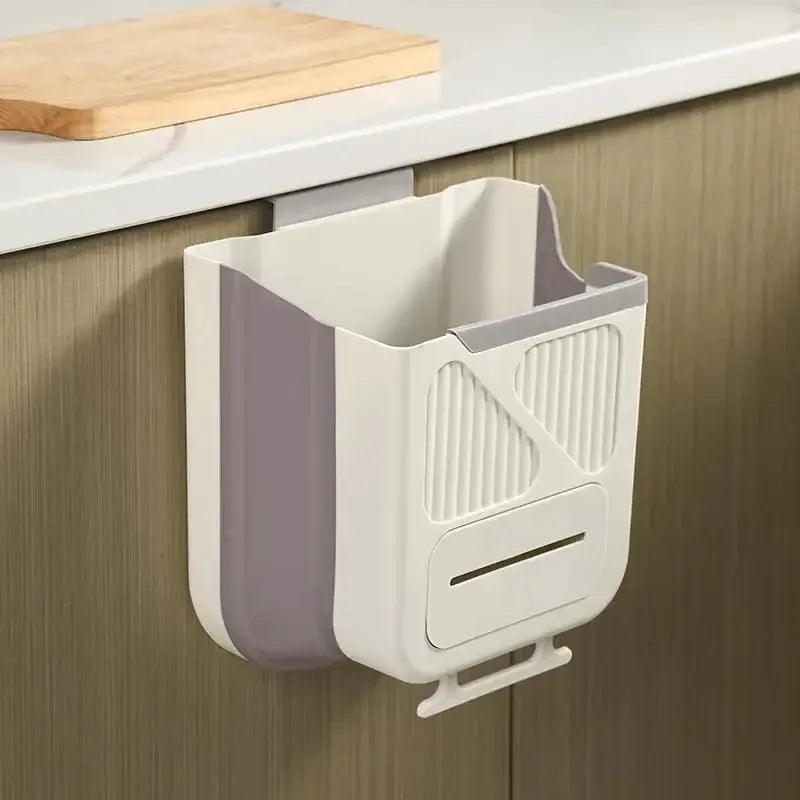 A white and gray foldable hanging trash can is mounted under a kitchen cabinet.