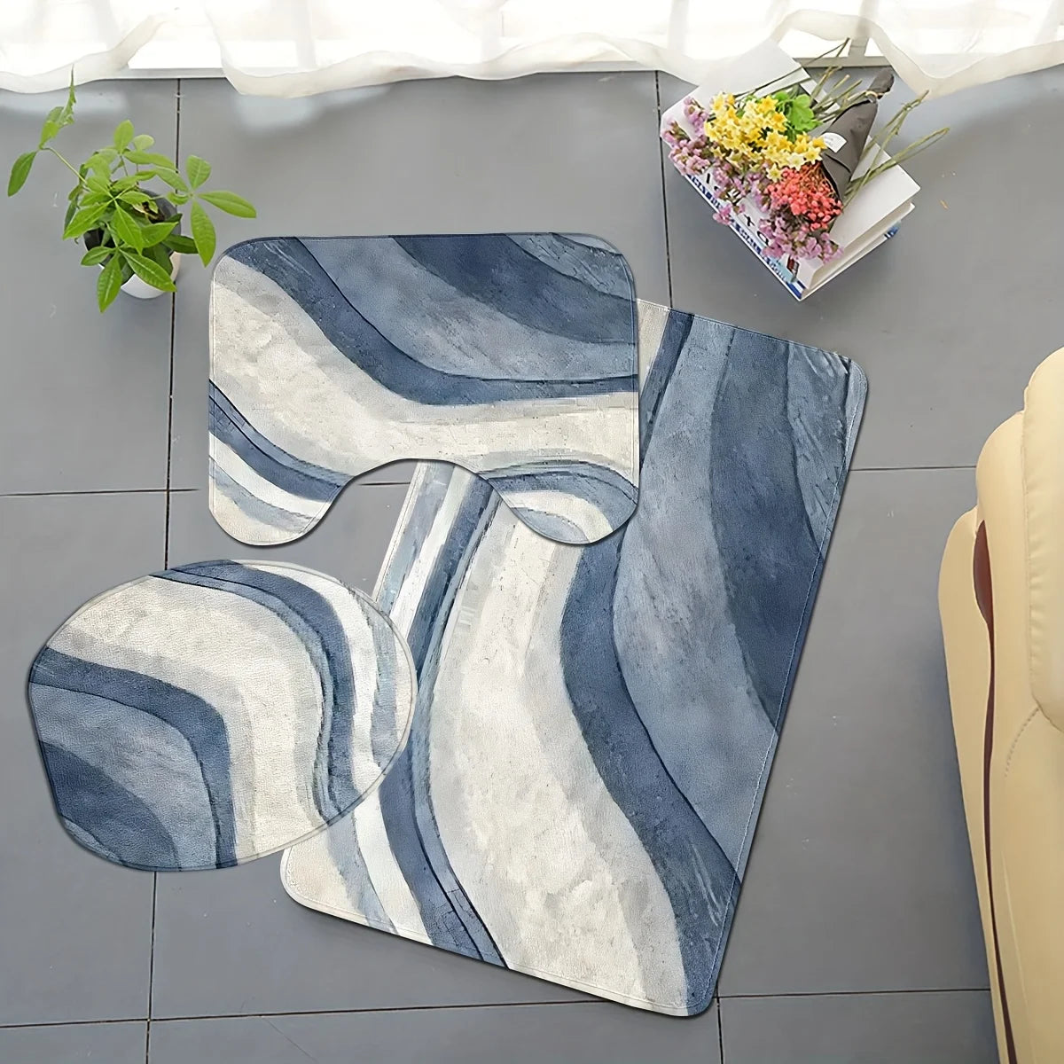 A set of three plush non-slip bathroom rugs featuring a U-shaped toilet mat and cover in blue and white stripes on a gray flo