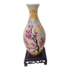 A ceramic vase decorated with pink and purple blossoms and gold accents, displayed on a dark wooden stand.