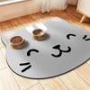 A gray mat shaped like a cat with white markings, used as a non-slip feeding mat for water bowls.