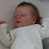 A close-up photo of a lifelike 18 inch sleeping reborn baby doll with painted veins and a soft cloth body.