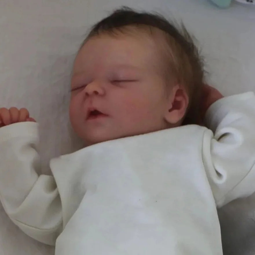 A close-up photo of a lifelike 18 inch sleeping reborn baby doll with painted veins and a soft cloth body.