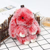 A fluffy red bunny keychain with a pom pom tail resting on a white grid background.