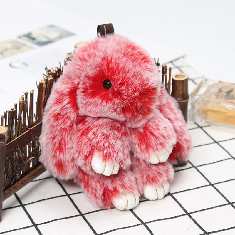 A fluffy red bunny keychain with a pom pom tail resting on a white grid background.