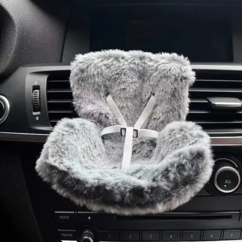 A fluffy gray faux fur decoration is placed in a car vent, featuring a criss-cross design.