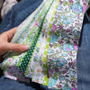 A hand holds a stack of 40-piece floral cotton fabric strips in various pastel colors for quilting and patchwork.