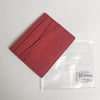 A reddish-pink genuine leather slim card holder wallet in a transparent plastic sleeve.