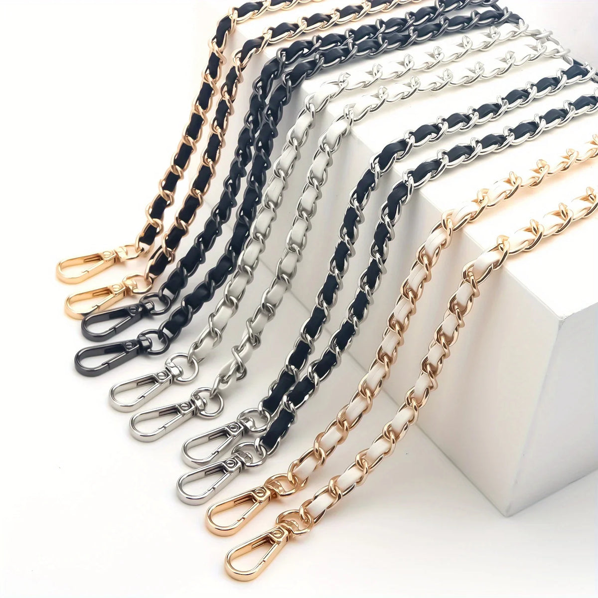 A collection of classic metal chain purse straps in black, silver, and gold tones laid out on a white surface.