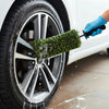 A hand using a green wheel barrel brush to clean the rim of a car tire.