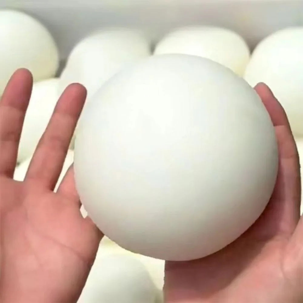 Eine Hand hält einen glatten, weißen Stressball-Fidget-Ball vor einem Hintergrund ähnlicher Bälle.