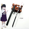 A miniature replica of a Demon Slayer katana sword with a black handle and pink hilt, displayed next to an anime-style female
