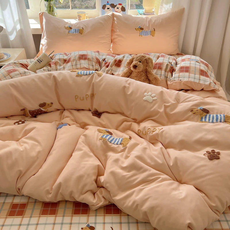 A set of pink and beige cartoon embroidered duvet covers featuring dog motifs and paw prints.