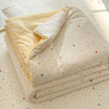 A stack of light beige quilt fabric featuring a colorful cartoon pattern with stars and lines, laid on a white quilted surfac
