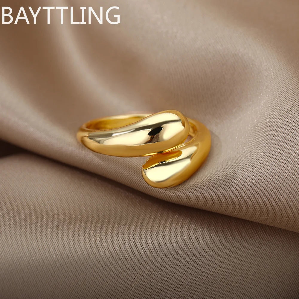 Primer plano de un anillo en forma de lágrima abierto en plata de ley con detalles dorados, sobre tela beige.