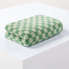 A folded green and cream plaid cotton bath towel set resting on a white surface.