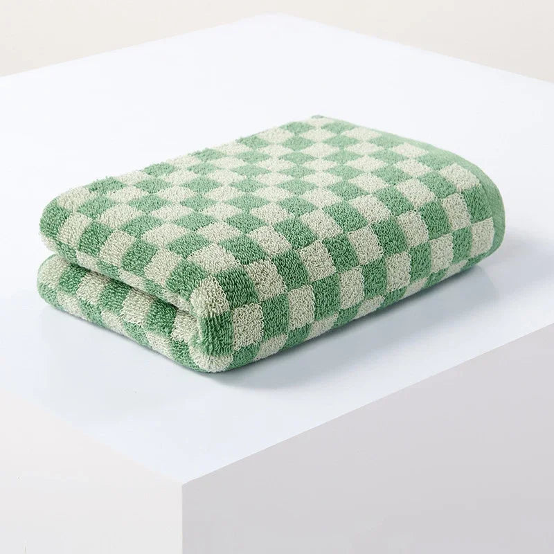 A folded green and cream plaid cotton bath towel set resting on a white surface.