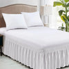 White elastic wrap-around bed skirt with ruffles and white pillows on a bed.