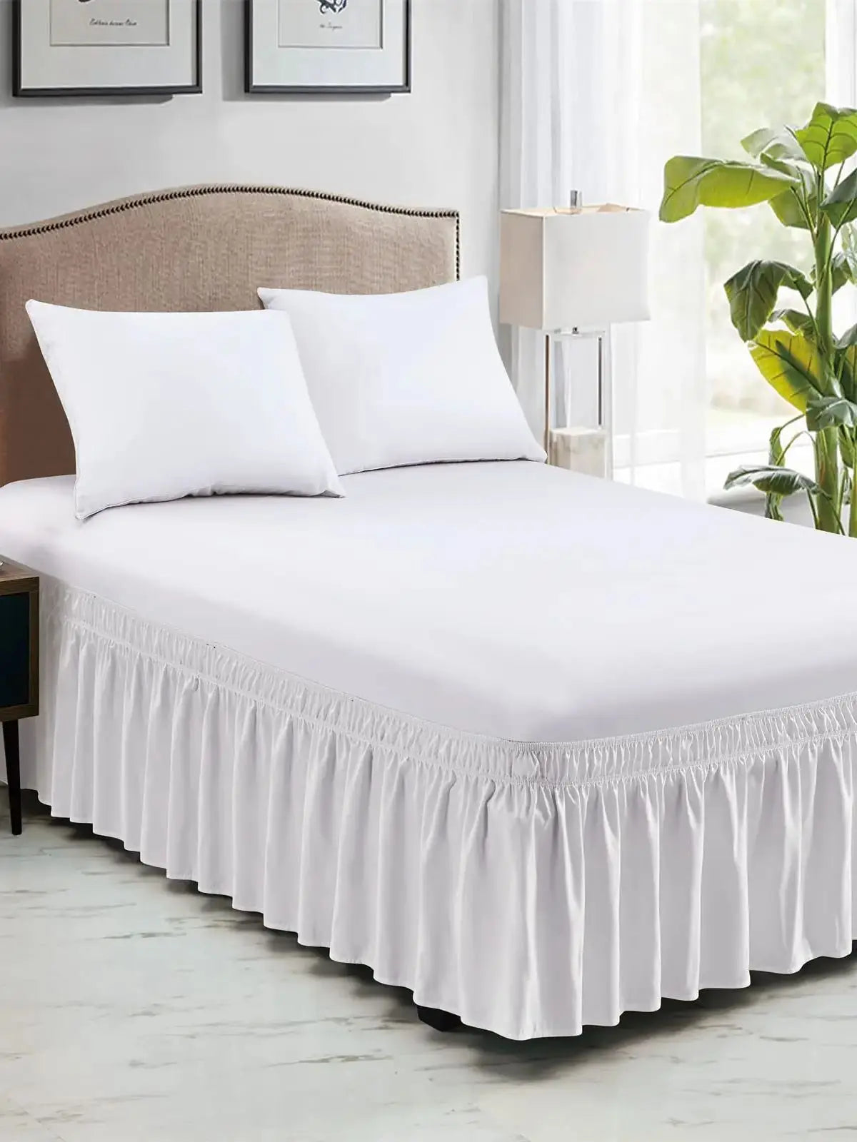 White elastic wrap-around bed skirt with ruffles and white pillows on a bed.