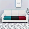 A white sofa slipcover featuring three colored cushions: teal, black, and red, placed on a patterned rug.