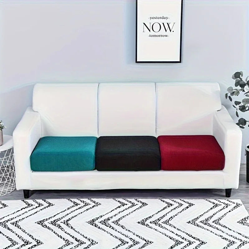 A white sofa slipcover featuring three colored cushions: teal, black, and red, placed on a patterned rug.