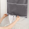A person is opening a gray wall-mounted laundry storage bag with multiple pockets, revealing white laundry.