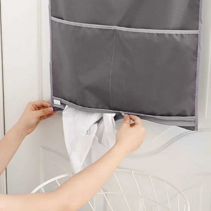 A person is opening a gray wall-mounted laundry storage bag with multiple pockets, revealing white laundry.
