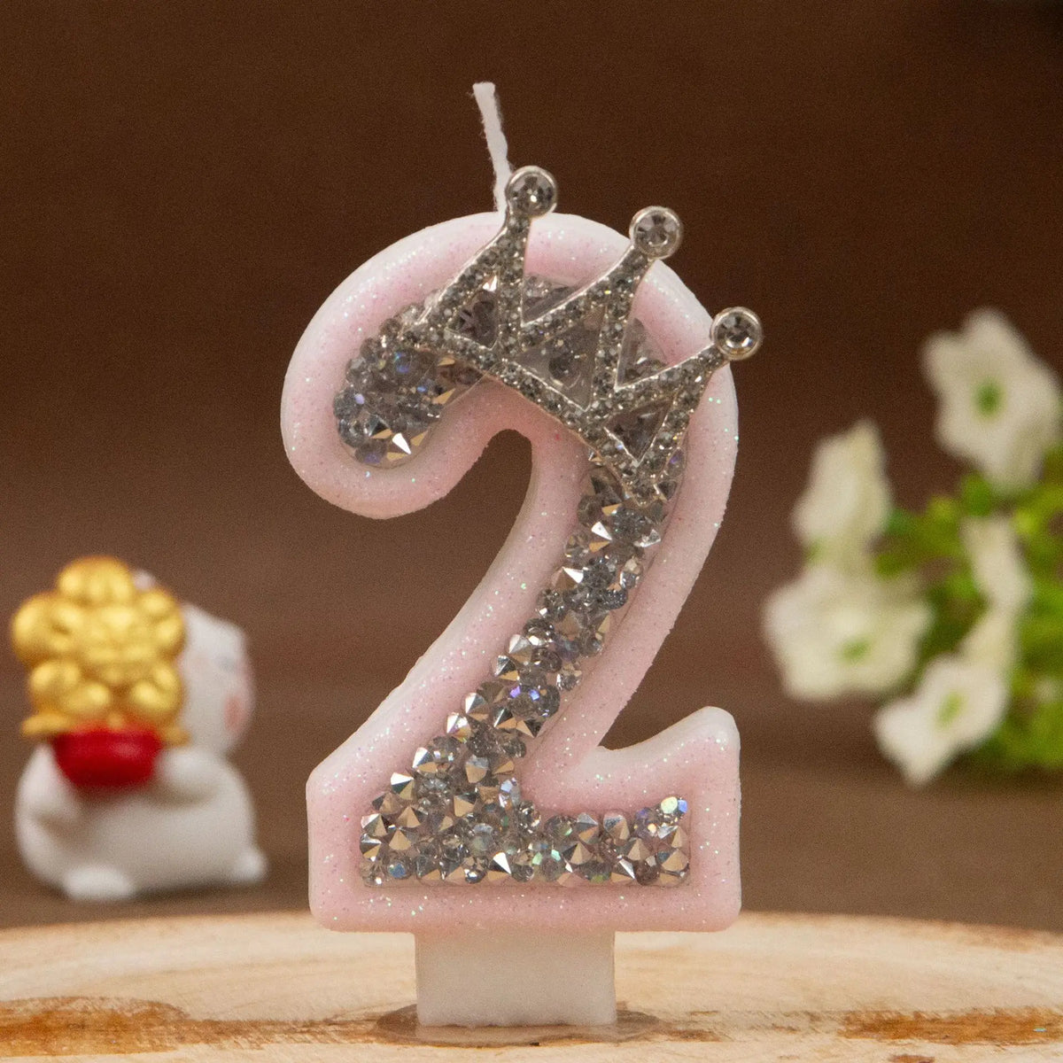 A pink number two candle decorated with silver rhinestones shaped like a crown.