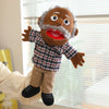 A hand puppet character with a gray beard and brown skin wearing a plaid shirt and tan pants is shown in a playful pose.