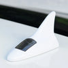 A white solar-powered shark fin antenna with a clear lens and LED safety light resting on a white surface.