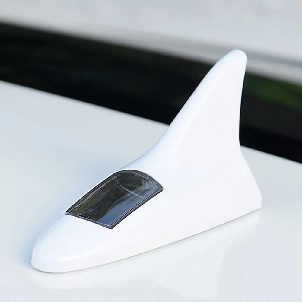A white solar-powered shark fin antenna with a clear lens and LED safety light resting on a white surface.