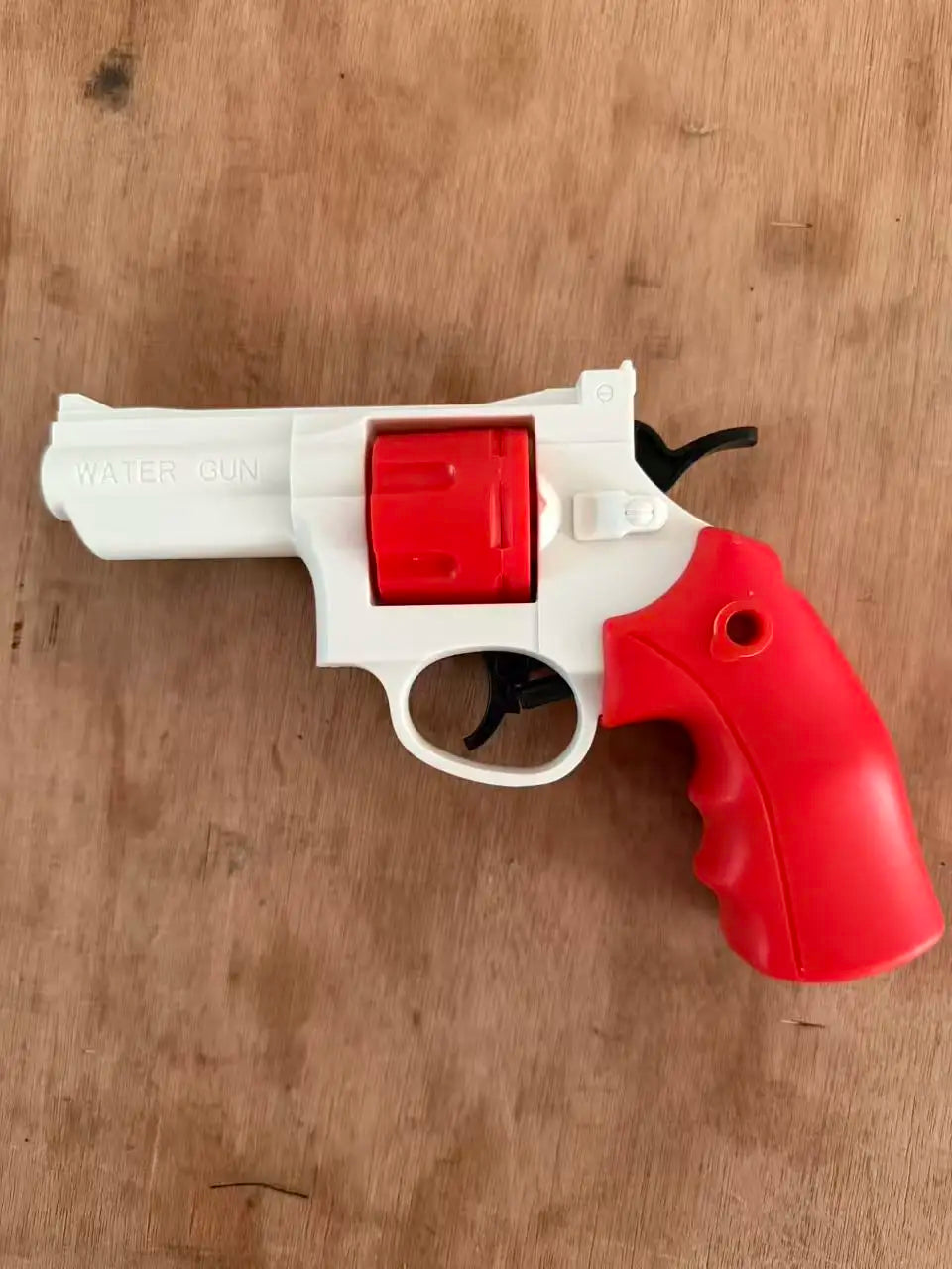 A white and red mini mechanical revolver water gun is shown on a wooden surface.