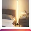 A modern white floor lamp with an RGB LED light illuminates a bedroom setting.